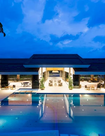 A luxurious, illuminated building at night with an expansive outdoor swimming pool in the foreground and modern seating areas.