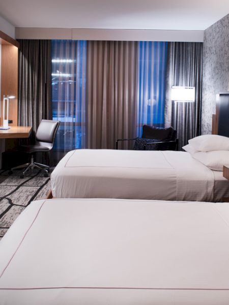 A modern hotel room with two beds, a desk, a TV, and stylish decor.