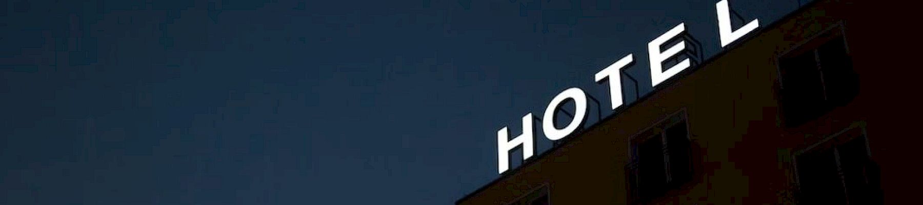 The image shows a building at dusk or night featuring a neon "HOTEL" sign on the roof.