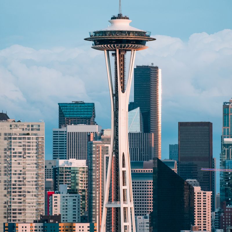 The image shows the Space Needle, a famous observation tower in Seattle, with the city skyline and various high-rise buildings in the background.