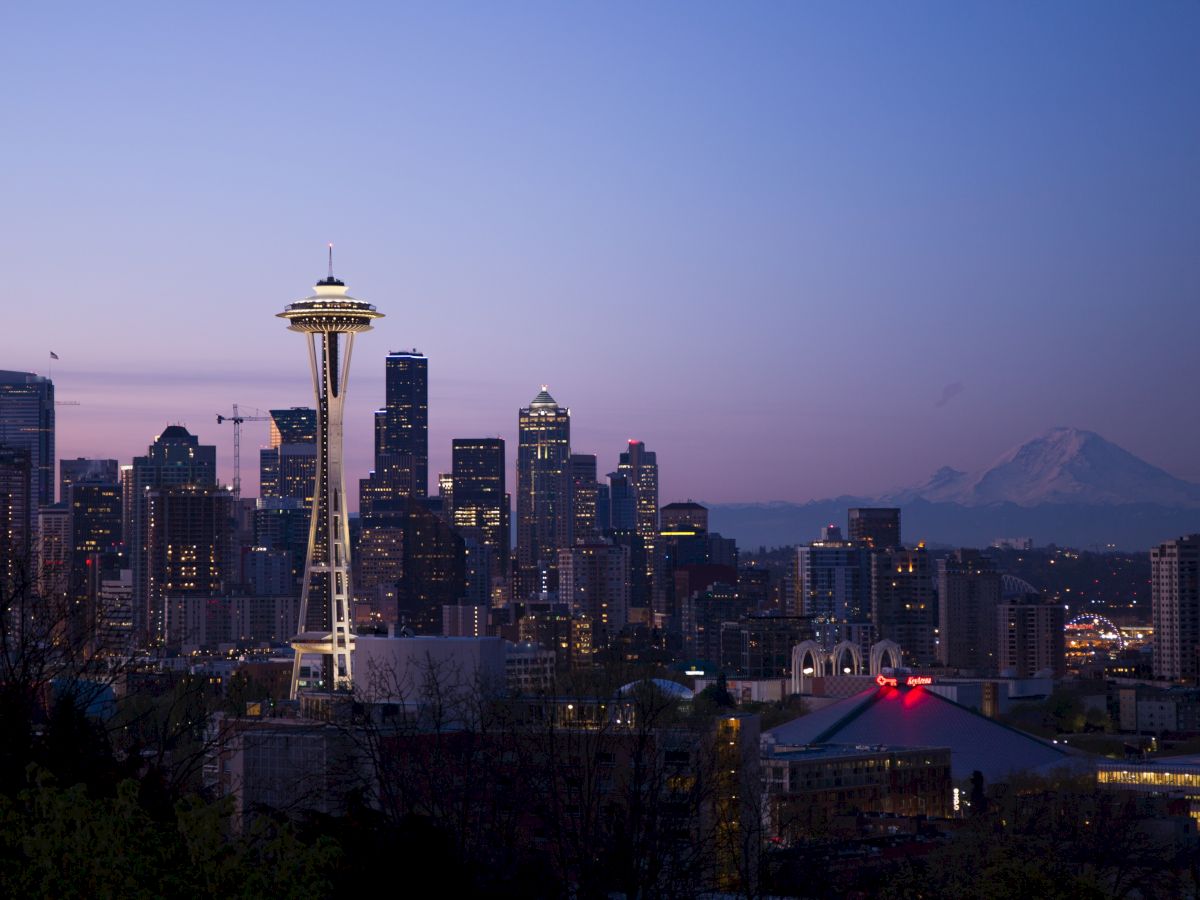 The image shows the Seattle skyline at dusk, with the Space Needle prominently visible and Mount Rainier in the distant background.